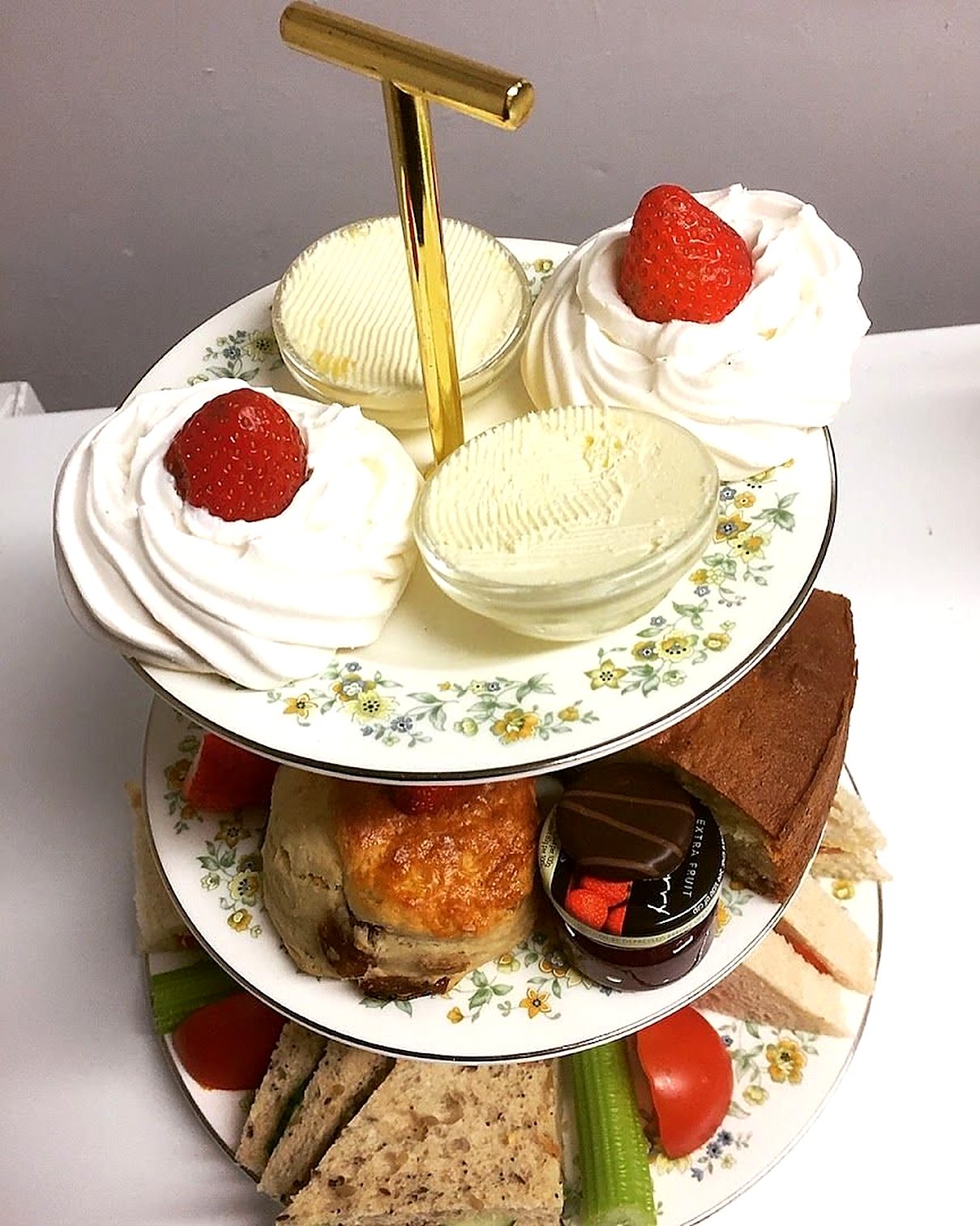 A three-tier cake stand: scones topped with cream and strawberries and pots of clotted cream on top, cakes and a scone in the middle, sandwiches and salad below